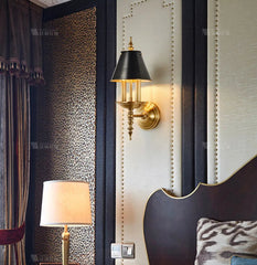 Decorative wall sconce and lamp in a bedroom setting with patterned wallpaper and headboard.