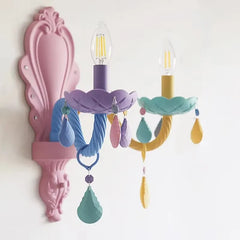 Close-up of a pastel-colored wall sconce featuring floral designs and hanging crystals, with a pink decorative backplate.
