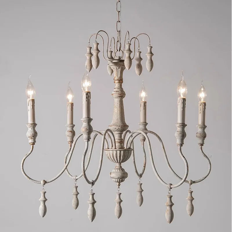 Close-up of a distressed white iron chandelier with candle-style lights and wooden accents, against a plain background.