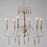 Close-up of a distressed white iron chandelier with candle-style lights and wooden accents, against a plain background.