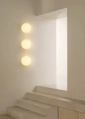 Three round white frosted glass wall lights mounted in a vertical line on a white wall near a staircase and an opening.