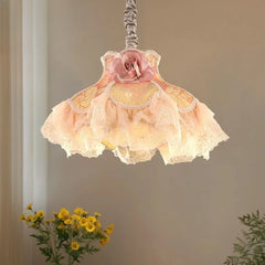 Close-up of a fabric pendant light with a pink rose accent and tiered, ruffled pink and yellow fabric shades.