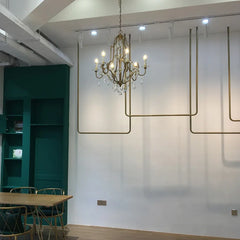 A gold candelabra crystal chandelier mounted in a modern space with a long wooden table and chairs.