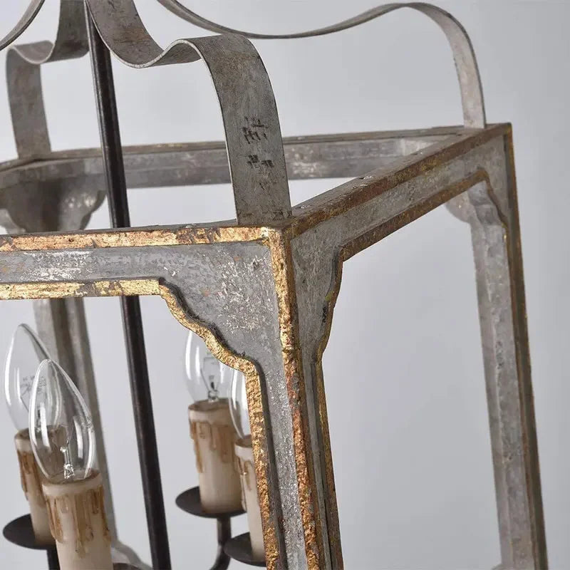 Detailed view of the four candelabra bulbs and the intricate frame of the distressed gray and gold lantern chandelier.