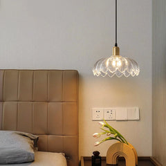 A bedside table with a hanging pendant light featuring a gold base and a floral glass shade, casting light on the wall and bedside.