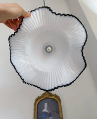 White light fixture with black rim held by a hand against a white wall with a portrait in the background.