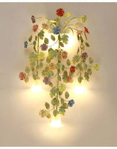Gold floral wall sconce with ceramic rose buds and clear glass shades illuminated against a white wall.