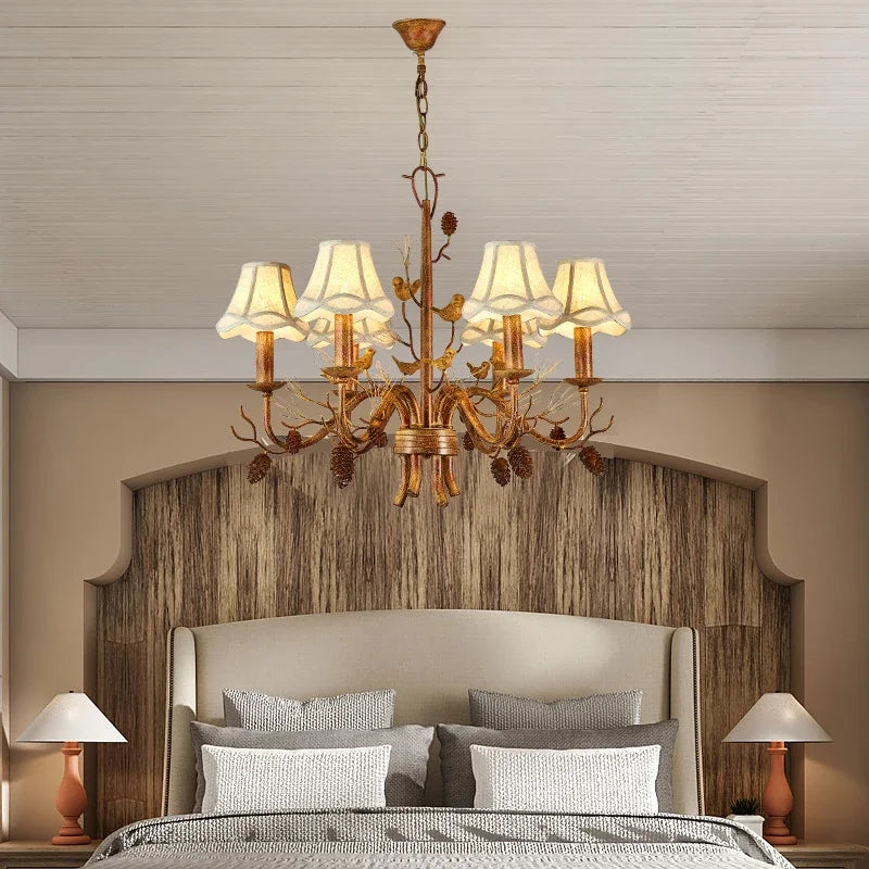 Bedroom setting featuring a gold chandelier with pine cone and bird embellishments, providing warm ambient lighting.