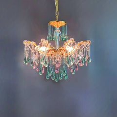 Close-up of a gold chandelier featuring numerous teardrop crystals in pink and green hues against a dark blue wall.