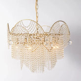 A close-up, front-facing view of a gold chandelier adorned with numerous clear crystals hanging in cascading strands and draped patterns against a white background.