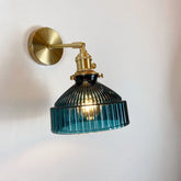 Blue fluted glass shade wall sconce with a brass arm and mounting plate against a white wall.