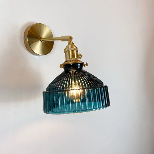 Blue fluted glass shade wall sconce with a brass arm and mounting plate against a white wall.