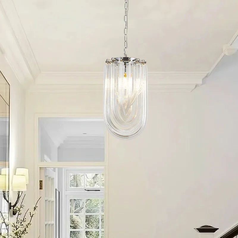 A single chrome U-shaped pendant light with clear glass tubes hanging in a hallway with a staircase.