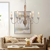A distressed wood and iron chandelier with six candle-style lights hanging over a sofa in a living room.