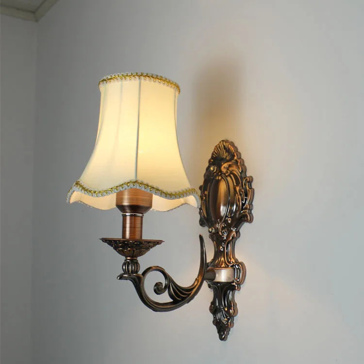 Close-up of a gold wall sconce with a textured cream fabric shade, showcasing the decorative base and arm.