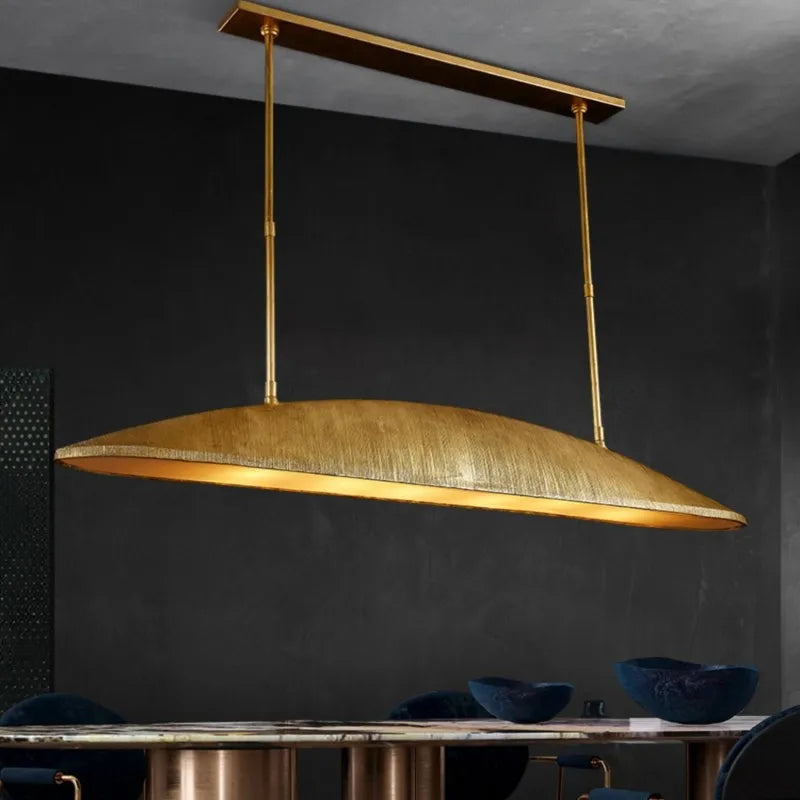 Gold linear pendant light with a textured finish hanging over a dining table