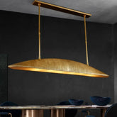 Gold linear pendant light with a textured finish hanging over a dining table