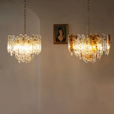 Two glass tube chandeliers with amber and clear glass tubes hanging on chains against a neutral wall with a framed portrait above.