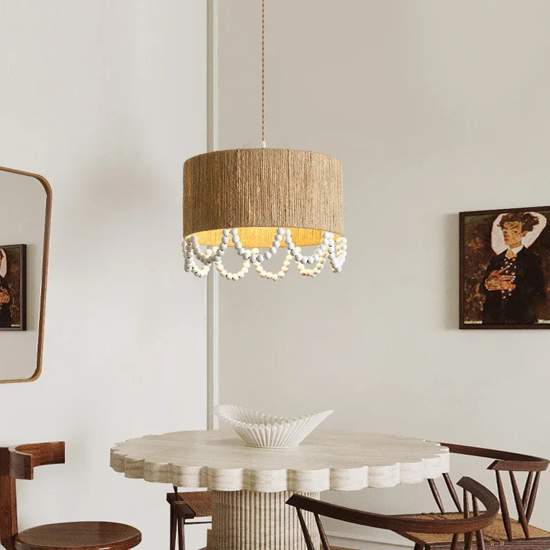 A rattan drum pendant light with a scalloped edge of wooden beads hanging over a round dining table.