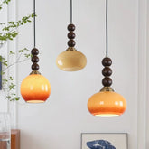 Three pendant lights with orange and brown shades hanging against a light gray wall.
