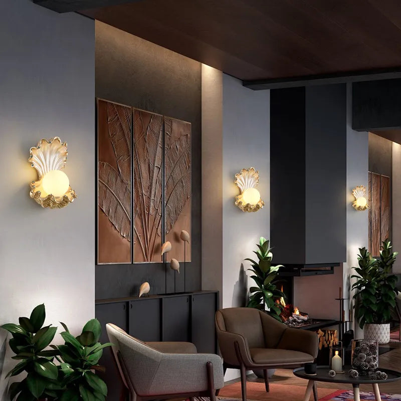 Two gold seashell wall sconces flanking a large textured artwork in a modern living room with a fireplace.