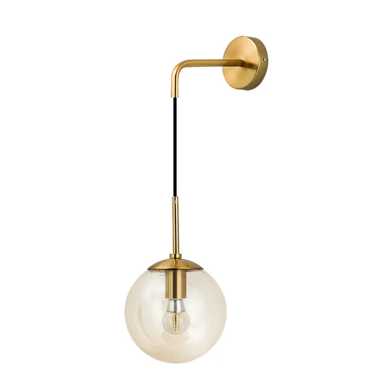A studio shot of a gold wall sconce with a clear glass globe and exposed bulb, showcasing a slightly amber tint.