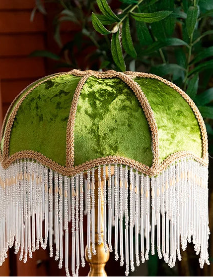 Green lampshade with fringes and decorative trim against a blurred natural background