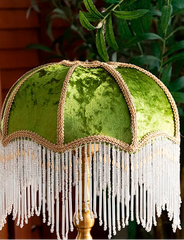 Green lampshade with fringes and decorative trim against a blurred natural background