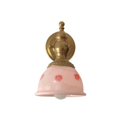 Vintage-style wall sconce with pink glass shade and brass fixture on a white background