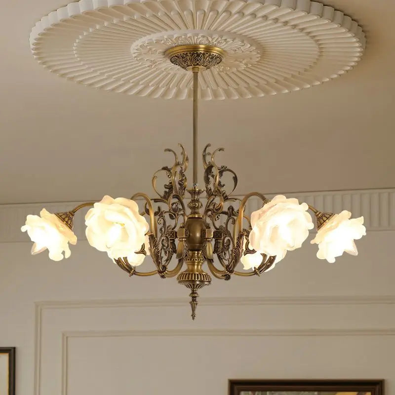 Polished copper floral chandelier with five rose-shaped glass shades, mounted on a white ceiling with ornate molding.