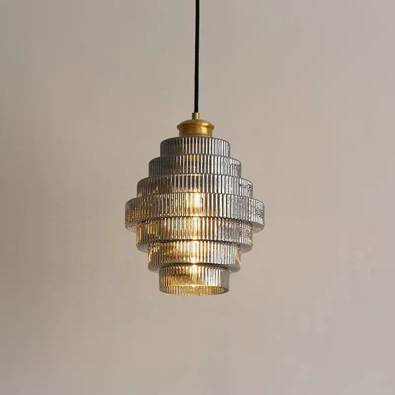 A close-up of a glass tiered pendant light with ribbed glass shades and a brass top, against a neutral background.