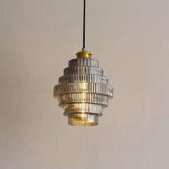 A close-up of a glass tiered pendant light with ribbed glass shades and a brass top, against a neutral background.