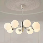 Close-up of a polished chrome sputnik chandelier with multiple frosted opal glass globes mounted on radiating arms, shown against a white ceiling with decorative molding.