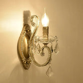 Gold crystal candelabra style wall sconce mounted on a beige wall, casting a warm glow.