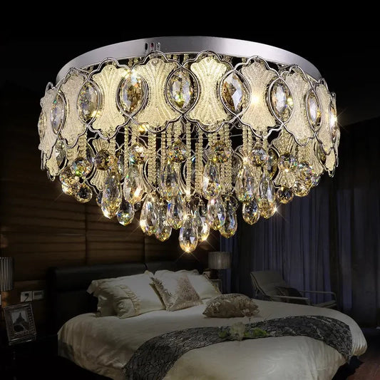 A luxurious chrome and crystal chandelier with teardrop-shaped crystals cascading from a tiered frame, installed in a bedroom above a bed.