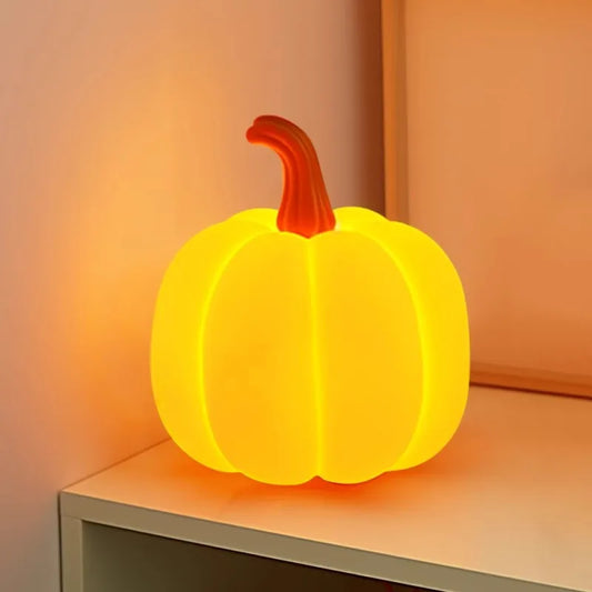 Illuminated orange pumpkin-shaped table lamp with a red stem, sitting on a white surface with a warm glow.