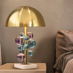 Gold and colorful crystal globe cluster table lamp with a marble base on a bedside table.