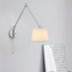 Chrome swing arm wall sconce with a white fabric drum shade and a pull chain, mounted on a white wall.