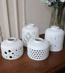 Set of four white ceramic lanterns with decorative patterns on a wooden surface.