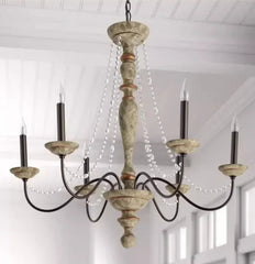 Vintage-style chandelier with wooden design and candle-like lights in a room with white walls.