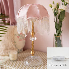 Decorative table lamp with pink shade and gold base on a checkered tablecloth.