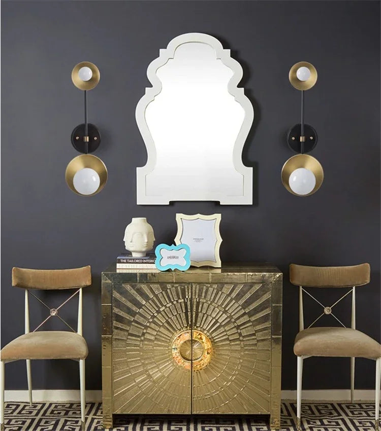 Decorative interior setting with a gold cabinet, mirror, and chairs against a dark wall.