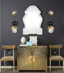 Decorative interior setting with a gold cabinet, mirror, and chairs against a dark wall.