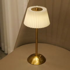 Table lamp with pleated white shade and gold base on a beige surface.
