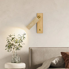 Wooden wall lamp on a neutral wall with a vase of plants and a bed in the foreground.