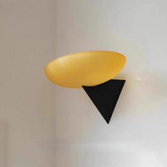 Side profile of a wall-mounted light fixture with a yellow frosted glass shade and a dark triangular base on a white wall.