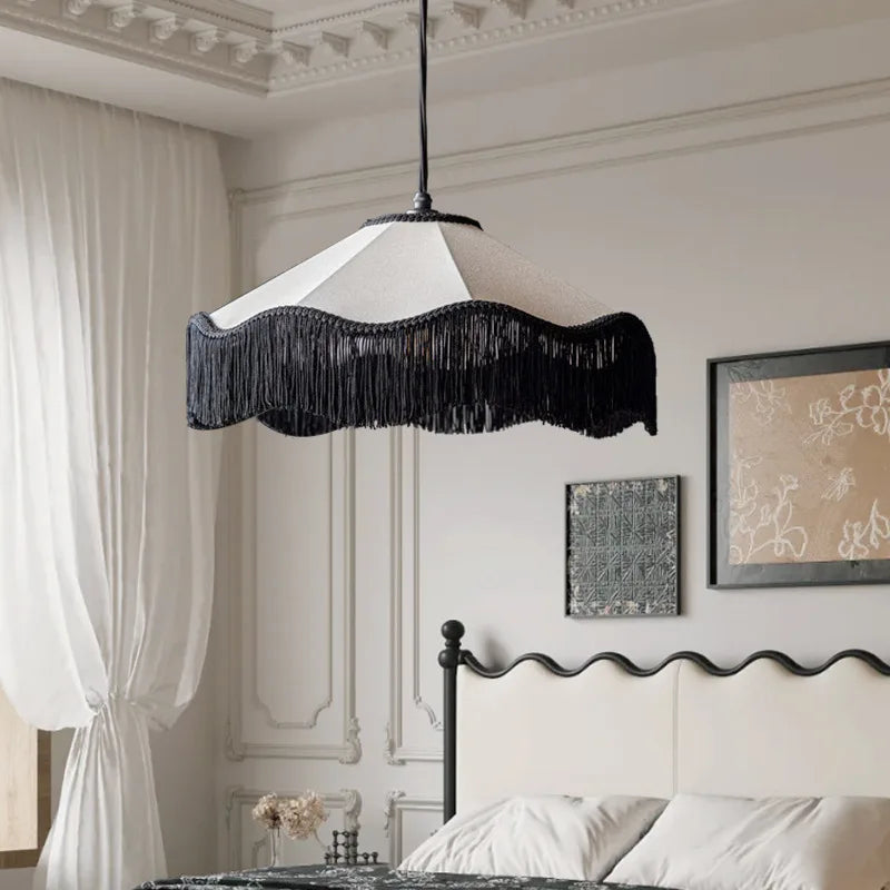 Fabric fringe pendant light with a white shade and black fringe, hanging in a bedroom setting above a bed.