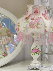 Decorative table lamp with floral design and pink beads on a white surface.