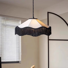 Black tassel fabric pendant light with a scalloped shade, suspended in a bright room near white blinds.