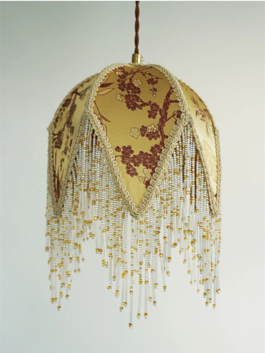 Decorative lamp with floral design and beaded fringe on a plain background